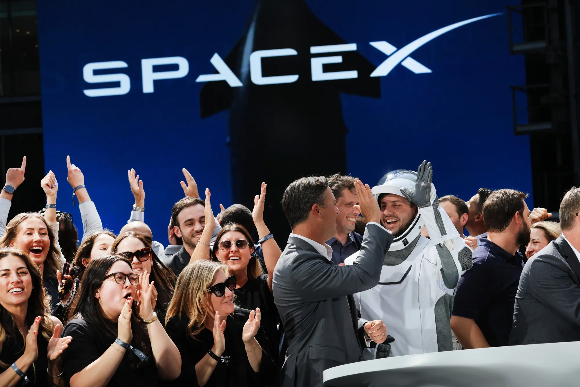 Employees celebrate in front of a SpaceX sign