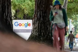 A Google office sign among trees with a pedestrian walking past