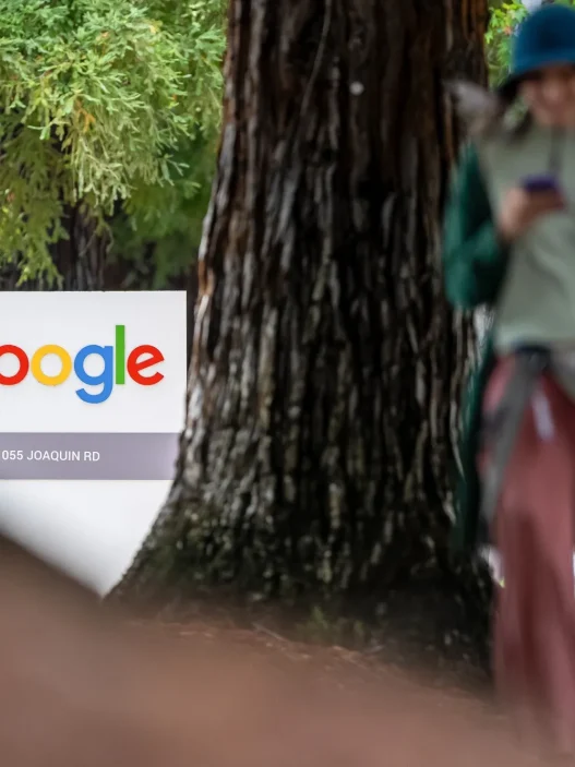 A Google office sign among trees with a pedestrian walking past