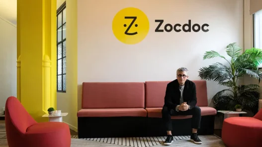 Zocdoc CEO Oliver Kharraz sitting on a couch beneath the Zocdoc logo