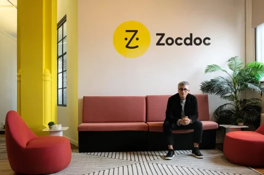 Zocdoc CEO Oliver Kharraz sitting on a couch beneath the Zocdoc logo