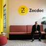 Zocdoc CEO Oliver Kharraz sitting on a couch beneath the Zocdoc logo